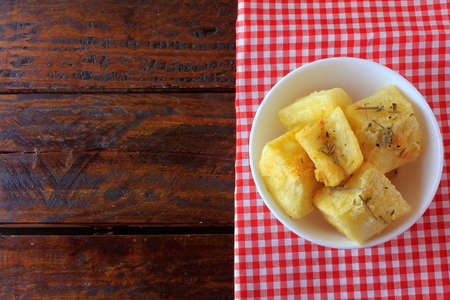 boiled and fried cassava (mandioca) in ceramic bowl on rustic wooden table in restaurantの写真素材