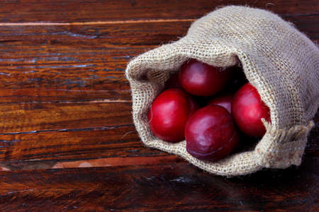 raw and fresh organic plums inside rustic fabric bag on wooden table. Close-up view.の写真素材