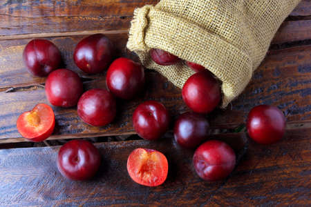 raw and fresh organic plums inside rustic fabric bag on wooden table. Close-up view.の写真素材
