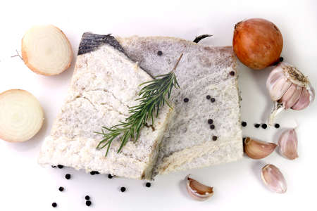 dry salted raw cod isolated over white background, accompanied by pepper, onion, garlic, parsley, spices. top viewの写真素材