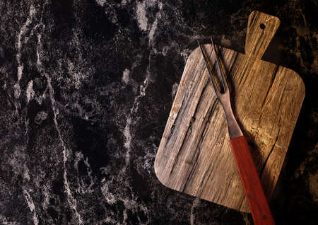 barbecue fork on Chopping cutting board isolated on black marble, in the vintage kitchen, with space for text. Top view. Background for steakhouseの写真素材