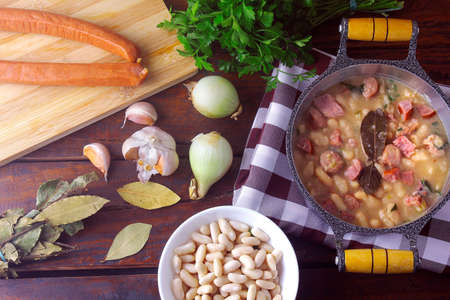 stew or white bean soup with sausage, vegetables, spices and herbs served in rustic pan on wooden table. Top viewの写真素材