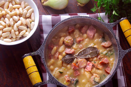 stew or white bean soup with sausage, vegetables, spices and herbs served in rustic pan on wooden table. Top viewの写真素材