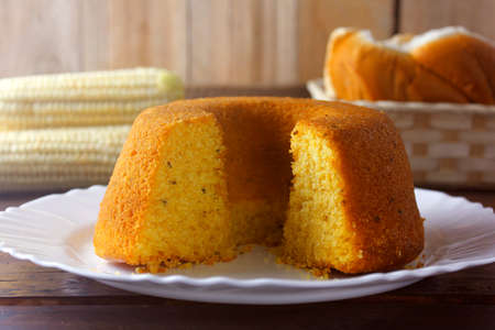 corn cake sliced on white plate on rustic wooden table. Typical Brazilian food. Front view....