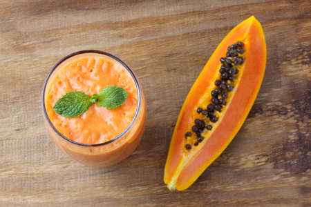 Homemade papaya smoothie with tropical fruits and mint in glass cup over rustic wooden table. top viewの写真素材