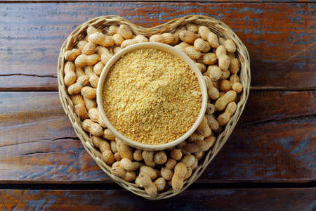 crushed and ground peanuts in ceramic bowl forming flour on rustic wooden table. organic food