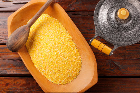 Raw cornmeal flour used in polenta, in wooden bowl over rustic wooden table. top viewの写真素材