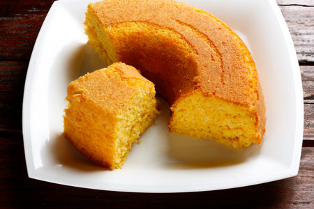 Corn Cake With Coconut on white plate on rustic wooden table. Typical Brazilian party food....