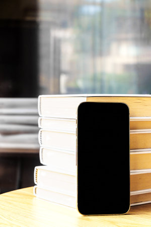 Smartphone with empty screen, next to a stack of books. With copy space. Vertical.の写真素材
