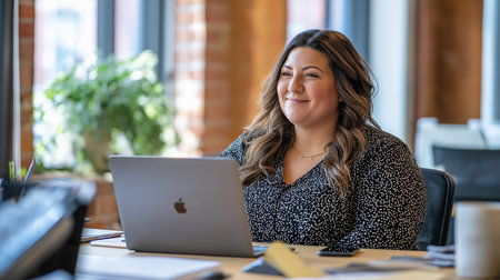 Fat women smiling while working on a laptop in a modern office. Confident businesswoman at her desk with a houseplant and natural light. Positive and professional work environment for fat womenの素材
