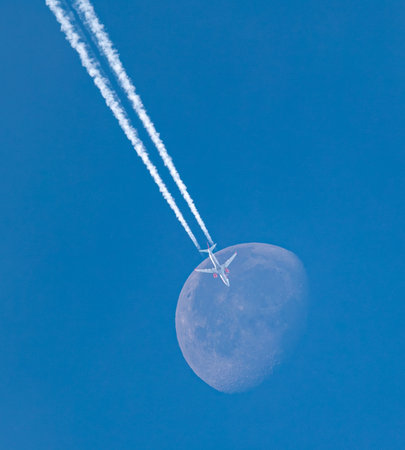 jet plane flying over the moon in the blue sky with contrailsの写真素材