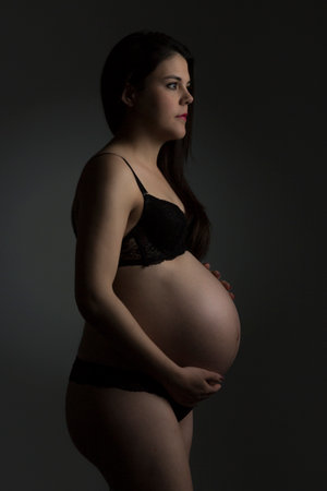 Pregnant woman in black lingerie on a dark background.の写真素材