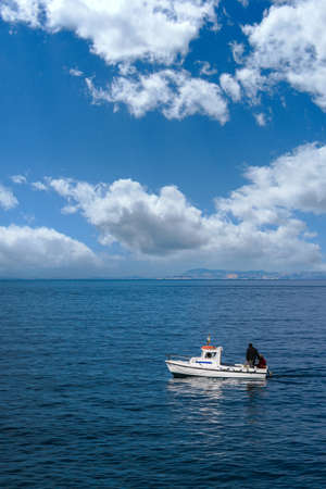 small lonely boat sailing the blue sea, mountains in the background and wonderful cloudsの写真素材