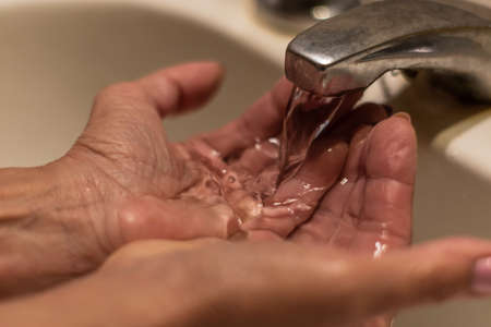 Hands of an older woman with painted nails on water running from a tap. She is washing her hands.の写真素材