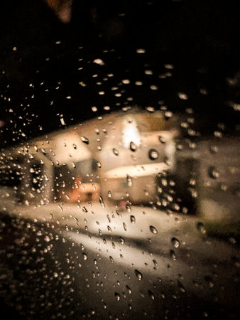 Water droplets on the glass, night light through the wet car window.