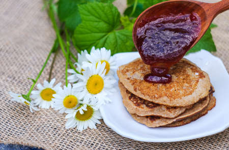 pancakes, tea with black currant on a green background. put jam on the pancakes. outdoors in a...