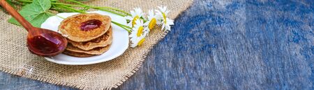 pancakes, tea with black currant on a green background. put jam on the pancakes. outdoors in a rustic style on a linen canvas fabric. next to daisies. long banner with copyspaseの写真素材