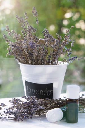 bouquet of dried lavender in white bucket with inscription. Natural blurred background. bottles with aromatic oilsの写真素材