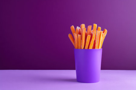 Frozen carrots in a purple plastic cup on a purple background.の素材