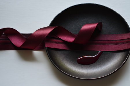 Red ribbon on a black plate with a spoon on a white backgroundの素材