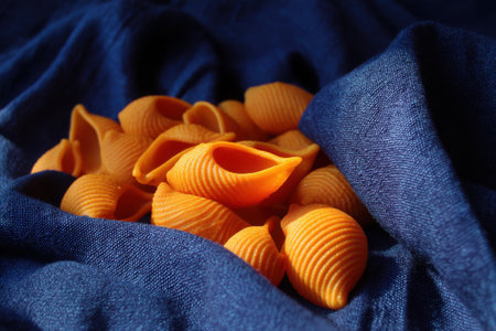 Close up of colorful pasta shells on blue fabric background. Selective focus.の素材