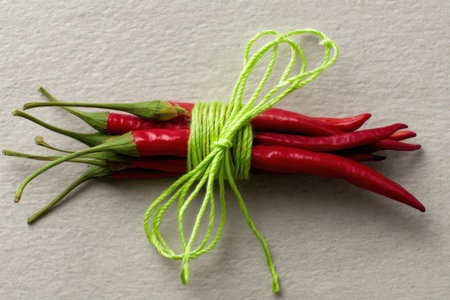 A bunch of red hot chili peppers tied with a rope on a white backgroundの素材