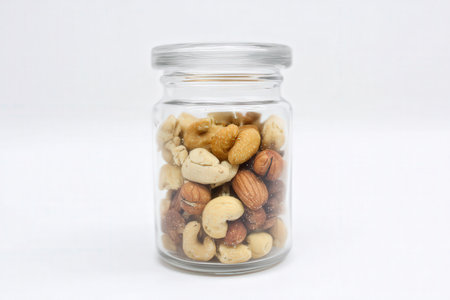 Mixed nuts in a glass jar isolated on white background. Healthy food concept.の素材