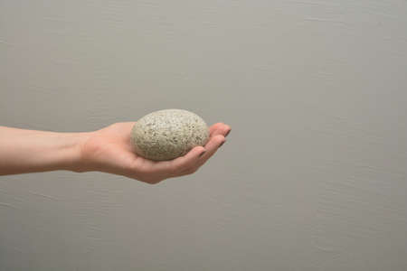 Female hand holds pebble rough stone with elliptic shape. Human palm offers natural object. Give a concrete piece.の写真素材