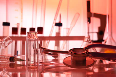 Chemical table with lab glassware and stethoscope in red colors. Test tubes, liquid flasks, medical gadgets in chemical laboratory. Biotech research laboratory with biochemicals on the lab desk.の写真素材