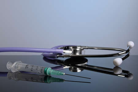 Inoculation syringe and medical stethoscope on a glass desk. Doctor gadgets with copyspace. Plastic...