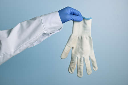 Doctor shows dirty white cotton glove. Medic hand with unhygienic protective fabric glove. Doctor hand wearing a blue nitrile glove holds another fabric. Blue gradient background.の写真素材