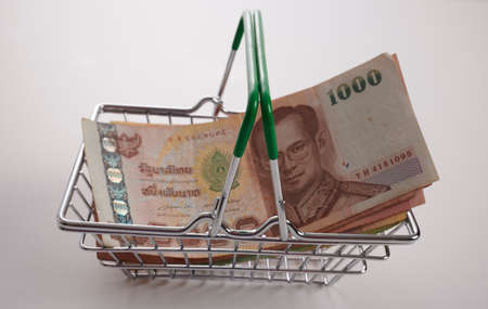 Thai Baht banknotes in a small shopping basket. Thai Bahts in a little metal cart. A lot of Thailand Baht paper bills are placed into a small toy shopping metal trolley. The concept of currency exchange. How to purchase Thailand paper money.の写真素材