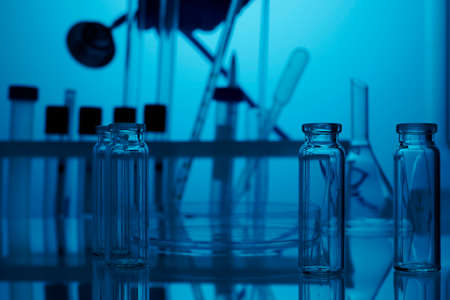 Empty lab glassware. Medical chemical lab with blue light background. Photo is taken in clinic laboratory with clean glasses on a table. Small glass vials and flasks without fluids on a chemical desk. Nobody on the photo.の写真素材