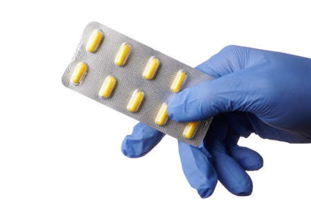 Blue gloved hand offers blister with yellow pills - isolated photo on a white background. Healthcare specialist offers yellow capsules of aid in the hand. Concept of medical ads for drug stores.の写真素材