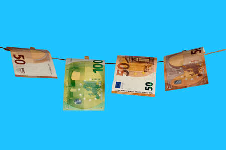 Euro banknotes on a rope. Cash laundry concept on a blue sky background. Clean money hung out to dry. EUR banknotes hanging on a string against blue background. Euro paper money on the rope.の写真素材