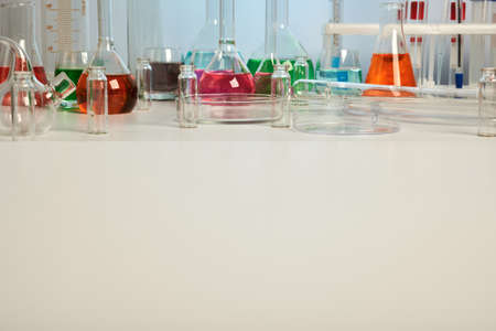 Lab glassware on white desk with copyspace. Clean desk surface for templates. Colored liquids inside chemical flasks, retorts, test-tubes. Scientific experiment for chemical investigations.の写真素材