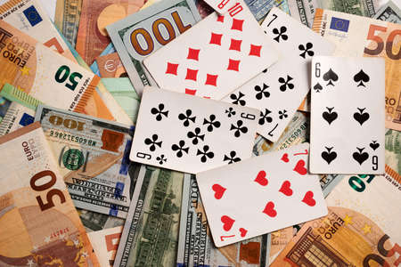 Playing cards on dollar and Euro bills. Dollar and Euro banknotes under gambling cards. Euro and dollar paper bills lay on background under casino and hazard symbols. Cost of gambling business.の写真素材