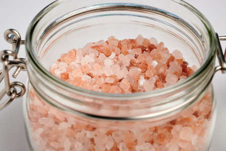 Rose salt crystals in glass container. Bottle with pink minerals. Himalayan salt crystals in open vial. Natural ingredients for cooking and bath. Red colored small stones.の写真素材