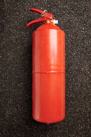 Fire extinguisher on ruberoid grain surface. Black textured background. Powerful emergency equipment...