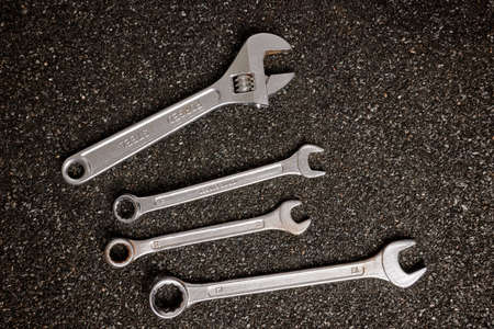 Metal wrenches on ruberoid mineral surface. Set of steel spanner tools. Workshop equipment for mechanics repair. Iron service toolkit. Setup wrenches made of chromed steel. Dark asphalted background.の写真素材