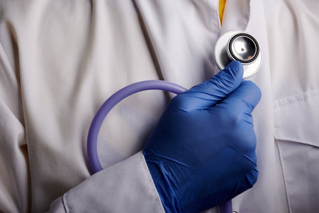 Doctor holds stethoscope in his hand. Medical gadget for advertisement medic staff. Nurse palm in blue nitrile glove with phonendoscope. Cardiology checking attributes. White dressing of medic guy.の写真素材