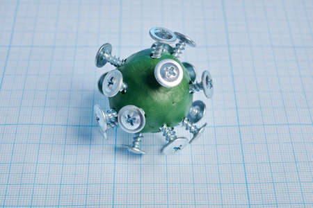 Plasticine virus model with screws- photo on a graph paper. Green plasticine virus model with metal chrome screws is laying on millimeter grid page. Simple viral model of flu pathogen.の写真素材