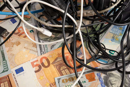 Computer cables - photo on money bank notes. Computer cables is laying on money bank notes. Dollars and Euro banknotes as background for electronics chaos. Price of network cords. Tangled wires.の写真素材