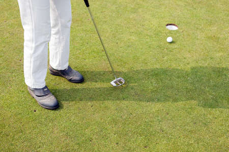 female in white trousers tries to putt the ball on the green of golf fieldの写真素材