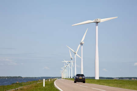 row of wind turbines and car on dike in The Netherlandsの写真素材