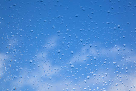rain drops on window pane and blue sky with white cloudsの写真素材