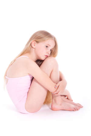 young girl in pink with sad expression sitting on floor of studio against white backgroundの写真素材