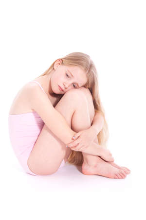 young girl in pink with sad expression sitting on floor of studio against white backgroundの写真素材