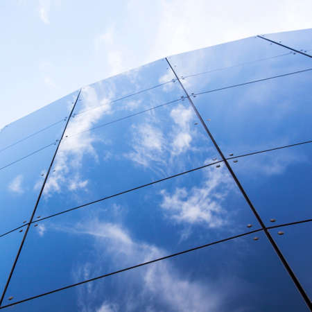 glass panes on facade of trade building reflecting blue sky and cloudsの写真素材