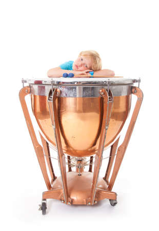 young boy resting his arms on kettle drum against white background in studioの写真素材